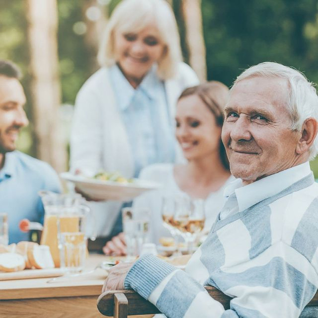 An elderly man enjoying quality time with his loved ones around a table, radiating warmth and togetherness.