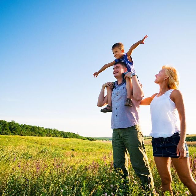A couple with a child stands in a field, enjoying the serene surroundings and the beauty of nature.
