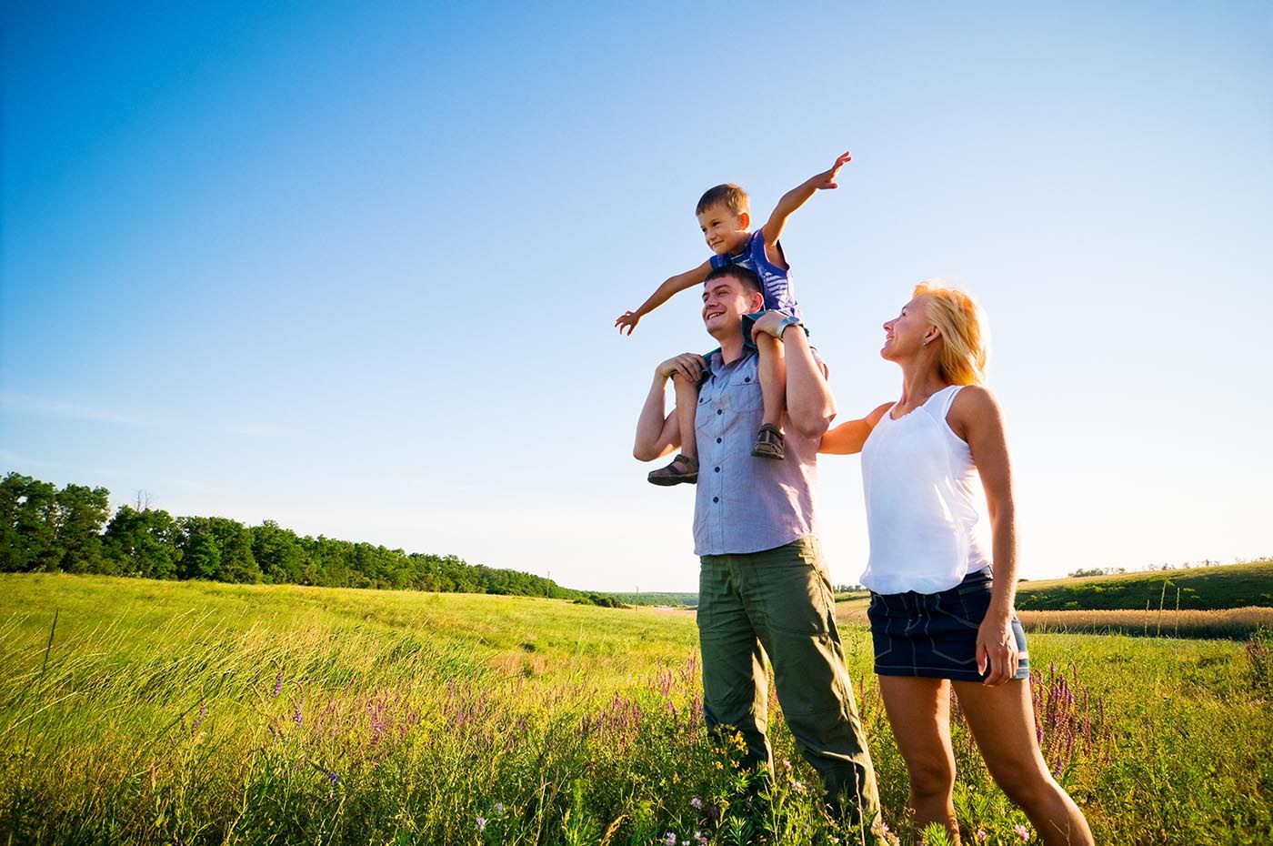 A couple with a child stands in a field, enjoying the serene surroundings and the beauty of nature.